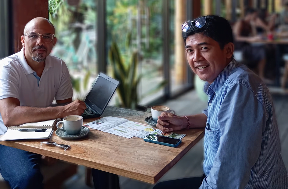 Two men setting on a table with a laptop and a cup of coffee discussing business. Bali Business Consulting