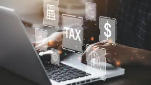 A person types on a laptop surrounded by floating icons related to taxes, including dollar signs, a tax form, and a globe, illustrating the comprehensive tax services they offer.