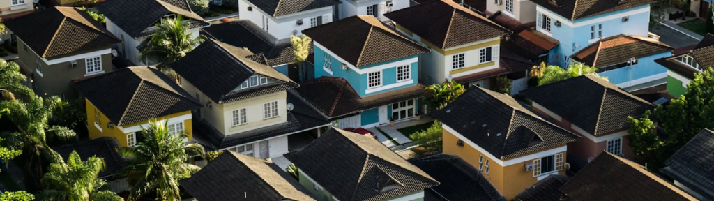 Aerial view of a residential area showcasing multiple two-story houses with dark roofs, distinctive colors, and surrounding greenery—a prime example of real world assets.